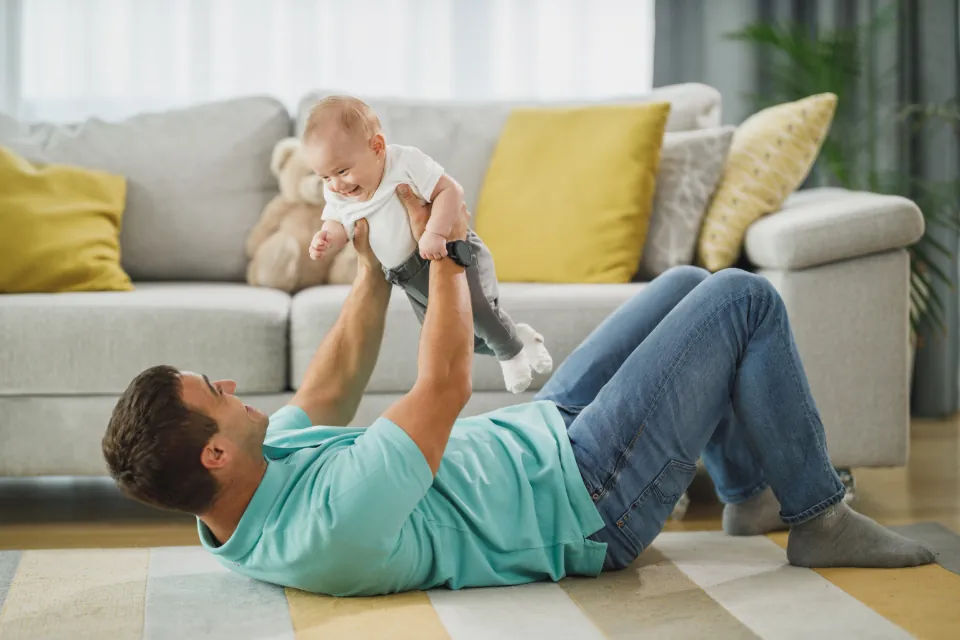 Un papa allongé sur le tapis du salon soulève son bébé à bout de bras